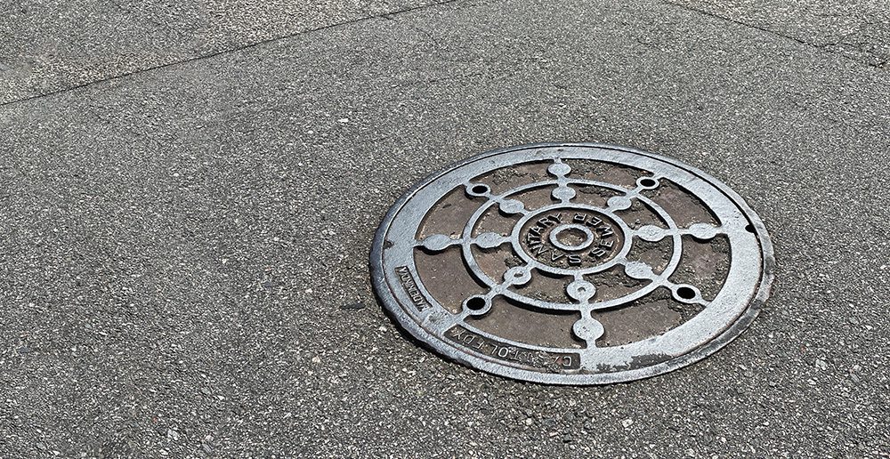 A manhole cover for a sanitary sewer system in an asphalt road.