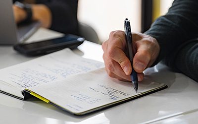 A businessman writing in a notebook with a pen.