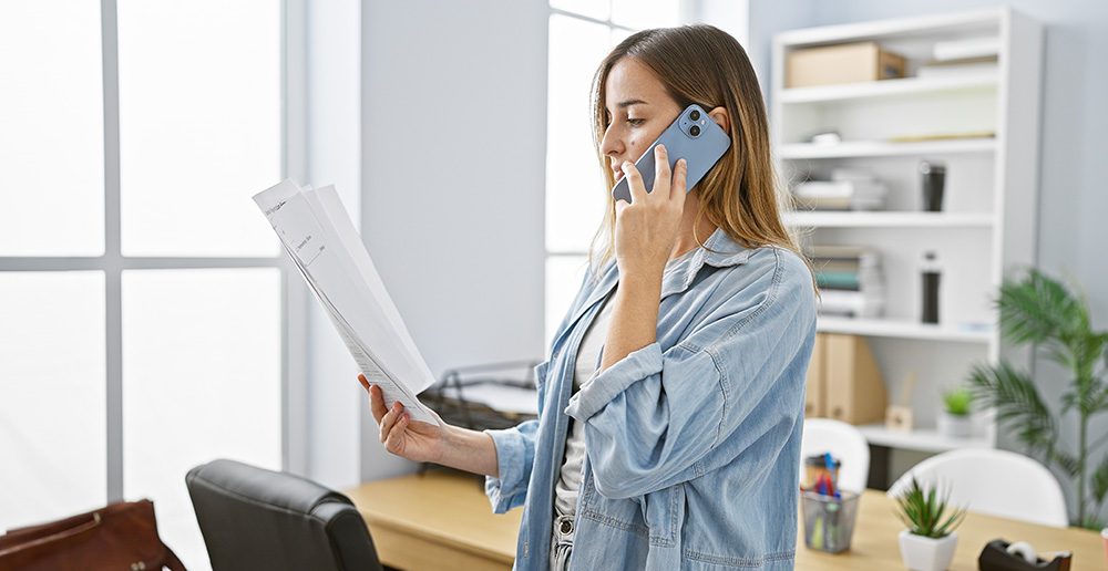 Concerned woman going over paperwork on the phone at her office.