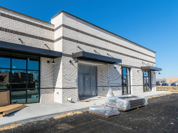 A white brick commercial property in a strip mall with road construction materials on the ground nearby.